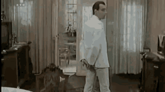a man in a white suit is standing in a living room in front of a door .