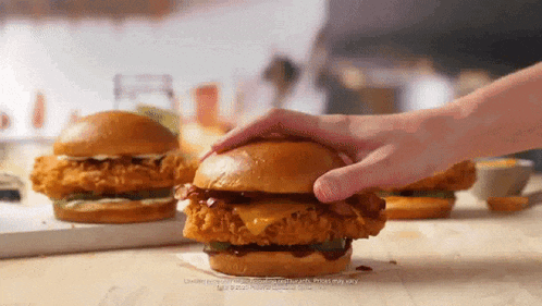 a person is holding a chicken sandwich on a wooden table