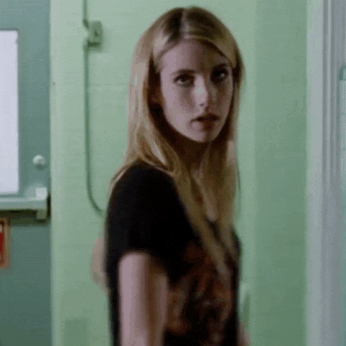 a woman in a black shirt is standing in front of a green wall and looking at the camera .