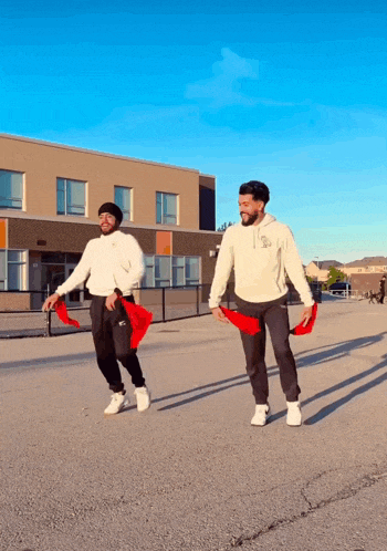 two men are walking down a street holding red scarves in front of a building with a blue sky in the background