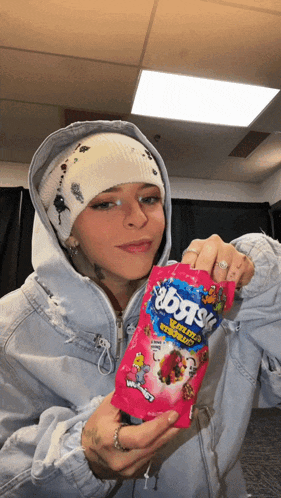 a girl in a hoodie holds a bag of swedish fish candy