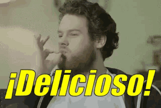 a man with a beard is eating a piece of food with the words " delicioso " behind him .