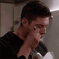 a man is applying makeup to his face while holding a pen in his hand .