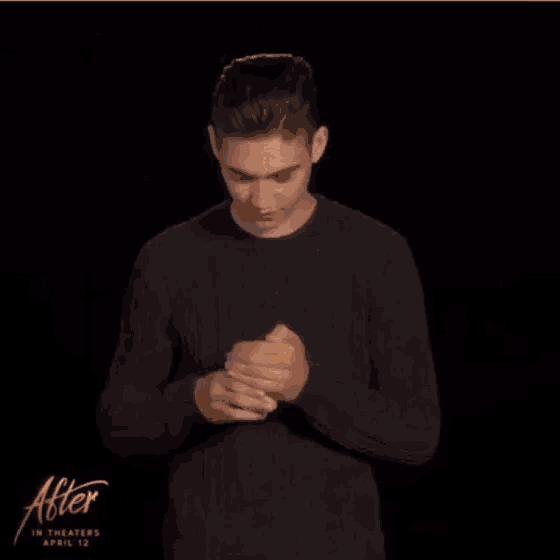 a young man in a black sweater is holding a cupcake with a toothpick in it .