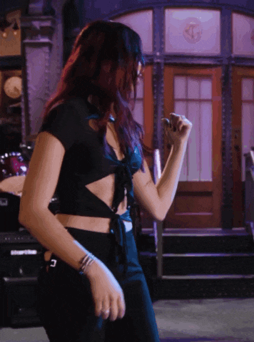 a woman in a black crop top and black pants is dancing in front of a building