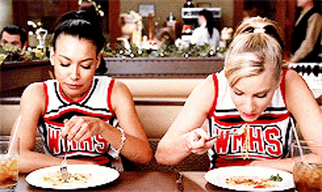 two cheerleaders wearing uniforms that say wmhs are eating