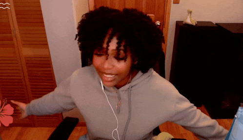 a woman wearing headphones and a gray hoodie smiles with her arms outstretched