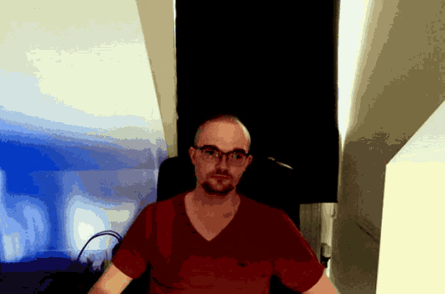 a man wearing glasses and a red shirt stands in a dark room