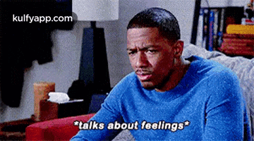 a man in a blue sweater is sitting on a couch talking about his feelings .