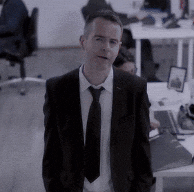 a man in a suit and tie is standing in an office with his hands in his pockets