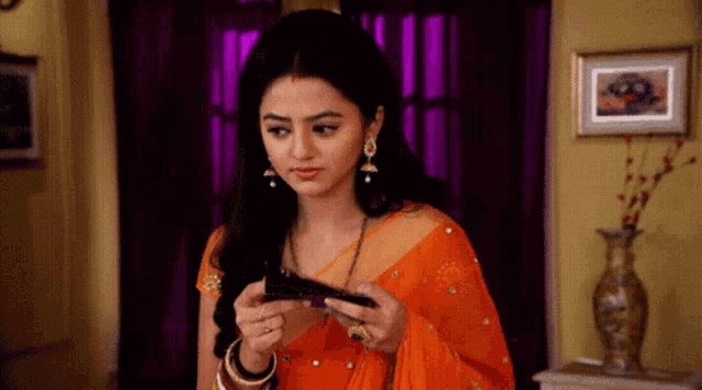 a woman in an orange saree holds a wallet in her hand