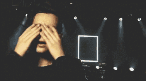 a man is covering his face with his hands on a stage with a square in the background .