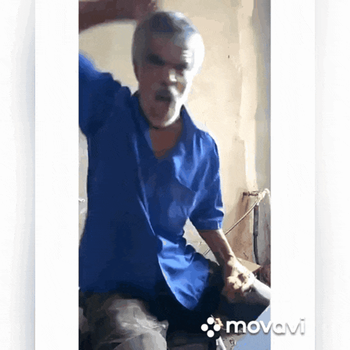 a man in a blue shirt is dancing in front of a white wall with the word movevi on the bottom