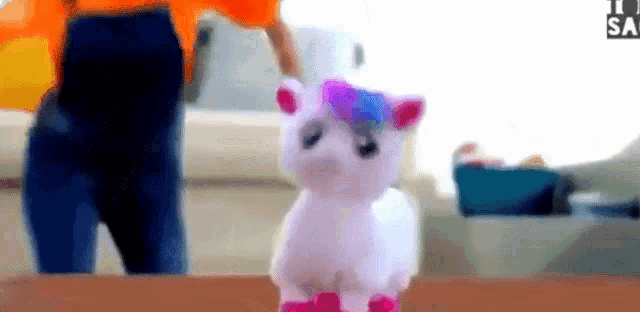 a stuffed unicorn with a purple and blue mane is sitting on a table .