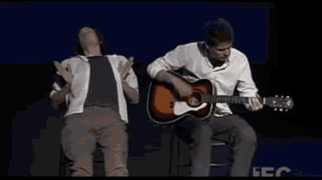 a man is playing a guitar while another man is dancing on stage