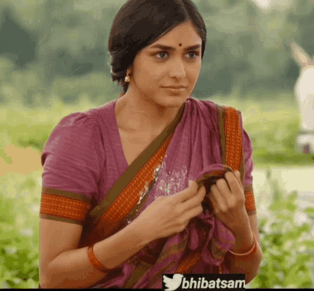 a woman in a purple shirt is standing in a field with a twitter logo in the upper right corner