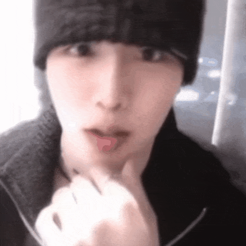 a close up of a person wearing a black hat and a black jacket with their tongue out .