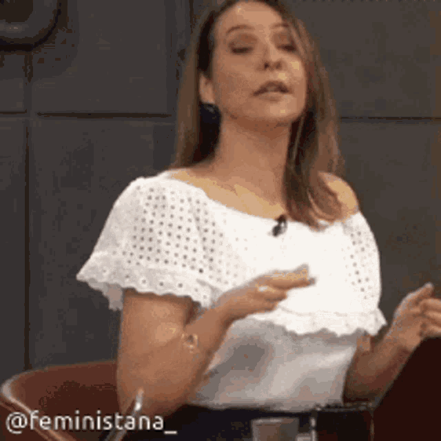 a woman in a white off the shoulder top is sitting in a chair and talking .