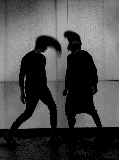 a black and white photo of two men dancing in front of a wall