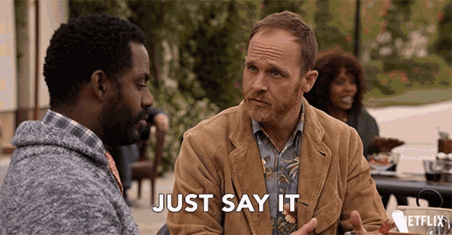 two men are sitting at a table with the words just say it written on the bottom