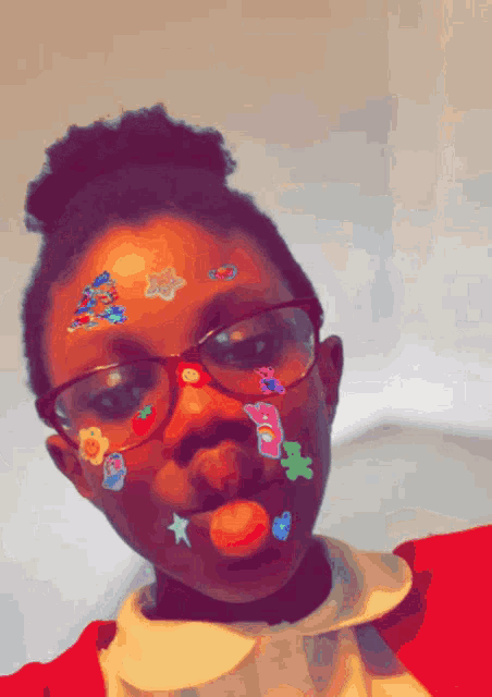 a girl with stickers on her face is wearing glasses and a red sweater