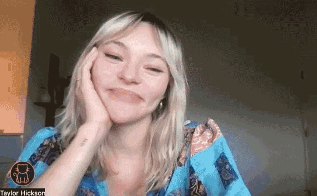 a woman in a blue shirt is making a funny face with her hand on her chin .