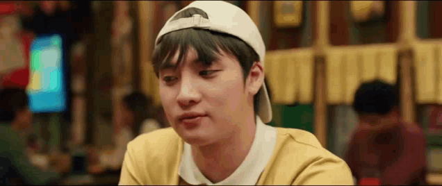 a young man wearing a white baseball cap and a yellow shirt is sitting at a table in a restaurant .