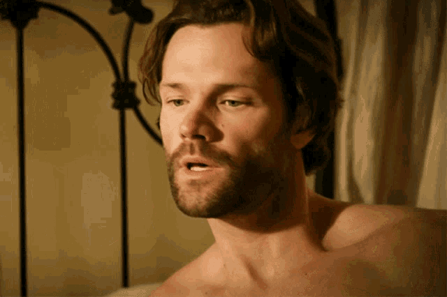 a shirtless man with a beard looks to the side