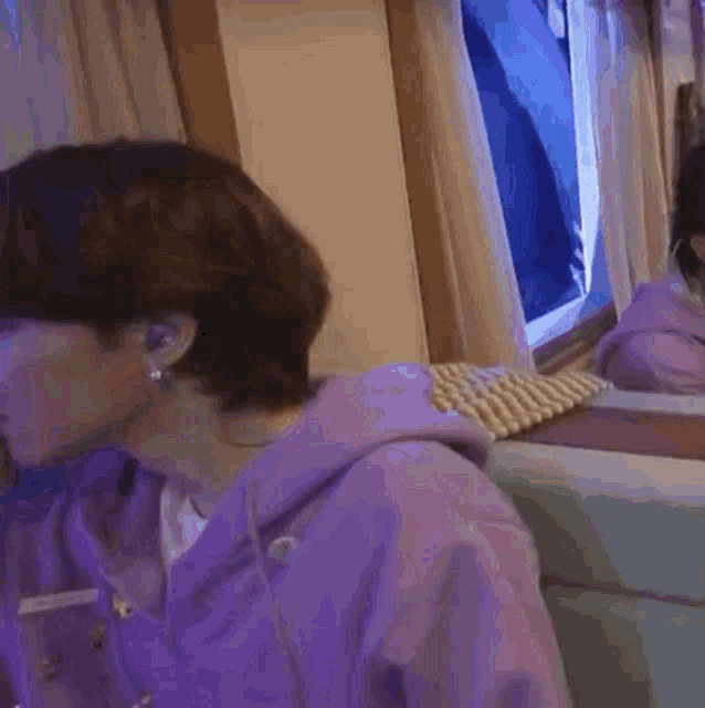 a woman in a purple hoodie is sitting in front of a mirror