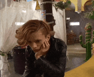 a woman in a leather jacket is sitting in a room with a cactus statue .