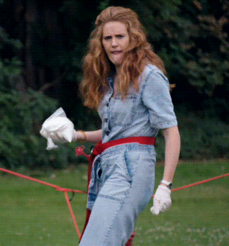 a woman in a denim jumpsuit is standing in a park