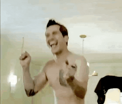 a shirtless man is holding a toothbrush in his hand and laughing in a bathroom .
