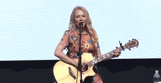 a woman singing into a microphone while holding a guitar that says fender on it