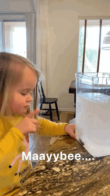 a little girl in a yellow shirt is playing with a container of water