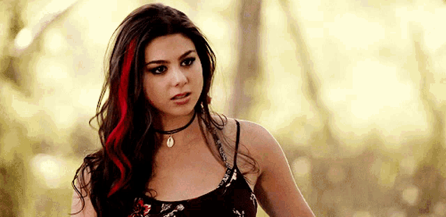 a woman with red streaks in her hair is wearing a choker necklace and a floral top .