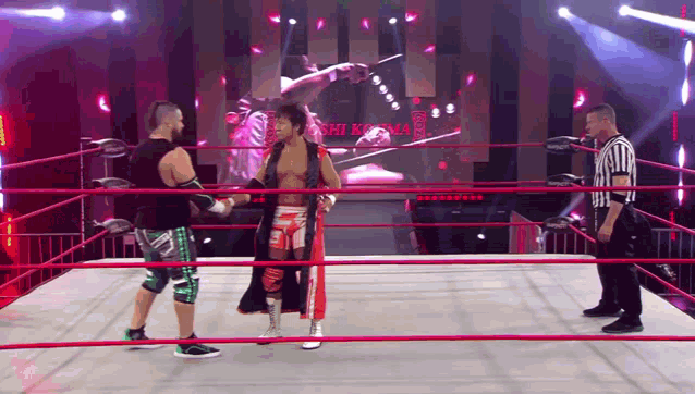 a referee stands in the middle of a wrestling ring with two wrestlers standing next to each other