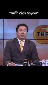 a man in a suit and tie is sitting at a desk in front of a television .