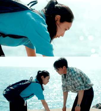 a man and a woman are looking at each other in front of the ocean