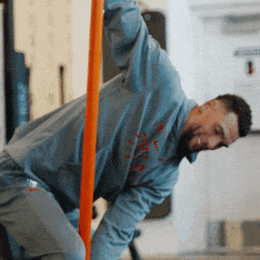 a man wearing a nike sweatshirt climbs a pole in a gym