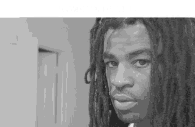 a black and white photo of a man with dreadlocks and a beard .