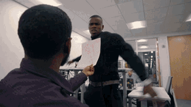 a man in a purple shirt is holding a piece of paper in front of another man in a black shirt