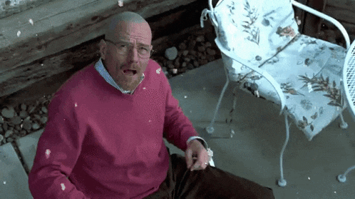 a man in a pink sweater and glasses is sitting on the ground
