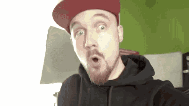a man with a beard and a red hat is making a surprised face .