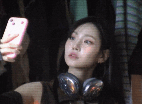 a woman wearing headphones is taking a picture of herself with her phone .