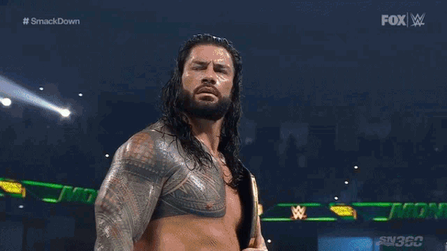 a man with long hair and a beard is holding a wrestling championship belt on a stage .