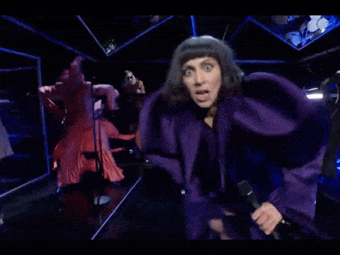 a woman in a purple suit sings into a microphone