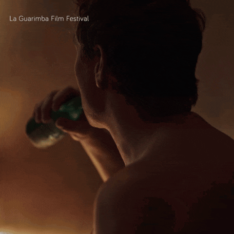 a man without a shirt is drinking from a green bottle with la guarimba film festival written below him