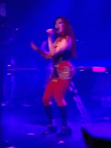 a woman in red pants is singing into a microphone on stage