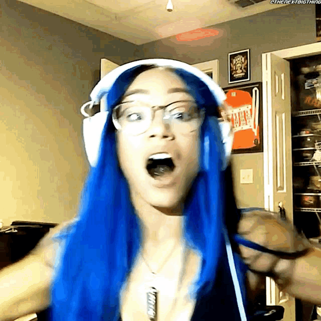 a woman with blue hair and glasses is wearing headphones and a necklace that says ' the next thing ' on it