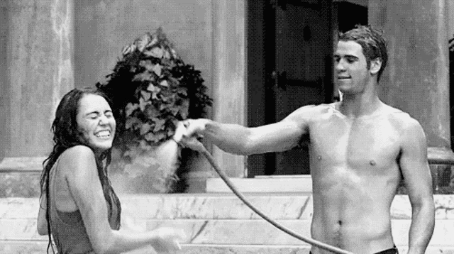 a man and a woman are playing with a garden hose .